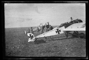 Nicht identifizierbare Ortschaft in Nordfrankreich oder Belgien: Kampfflugzeug mit Tatzenkreuz und Doppeldecker auf einem Feld (Nahaufnahme)