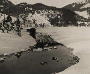 Winter in Oberbayern. Verschneite Landschaft. Eine Hütte an einem Bachlauf bei Schliersee.