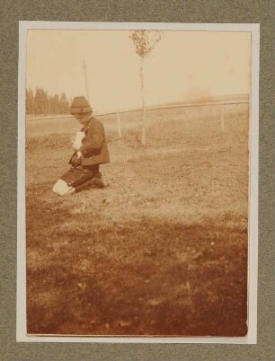 Raimund von Hofmannsthal mit einem Kaninchen auf einer Wiese in Aussee, knieend