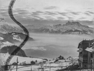 Berglandschaft : Blick in eine verschneite Berglandschaft. Im Vordergrund Häuser, im Hintergrund Gebirgszüge