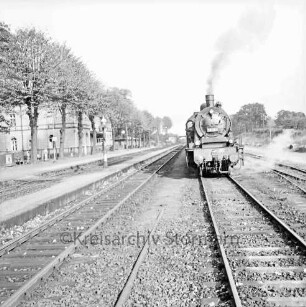 Bahnhofsgelände: Gleise mit Dampflokomotive: links Bahnsteige, Wasserkran, Baumreihe, Bahnhofsgebäude: Blick nach Norden: im Hintergrund Brücke Tremsbütteler Weg