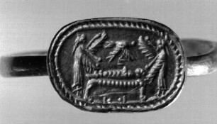 Fingerring: dünne Platte in Kartuschenform mit eingraviertem Bild: Toter (Osiris?), auf einer Kline liegend, darüber Seelenvogel, geflügelte Göttinnen zu Haupt und zu Füßen