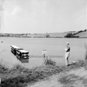 Moorteich mit Schulschwimmsteg: im Vordergrund rechts Junge am Ufer: hinten Knicklandschaft