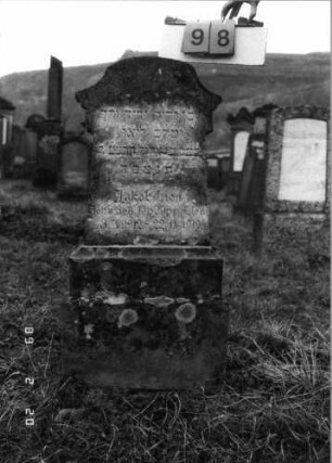 Grabstein 98 (Index: 99798525) Material: Sandstein Zustand: leicht verwittert Maße HxBxT: 114x36x15 cm Beschreibung: Stele mit überkragendem, rund eingezogenem Segmentbogenabschluß, Sockel: Grabstein 98