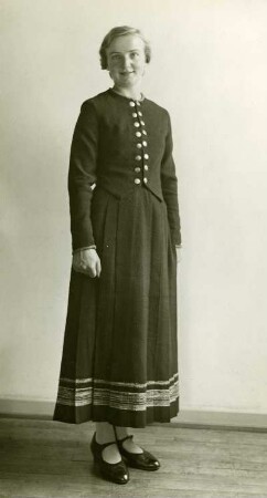 Frau stehend in Volkstracht mit handgewebtem Kleid. Frontal. Halbtotale