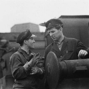 Zwei Eisenbahner zwischen Gleisen im Gespräch, im Vordergrund ein Hülsenpuffer (Serie Deutsche Reichsbahn - Brigade "Otto Buchwitz")