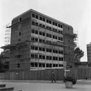 Hochhaus [später Gebäude B]: Mommsenstraße: Rohbau mit Gerüst: davor Bauzaun und Mann: rechts Betonsilo: dahinter Hauptgebäude [später Gebäude A]: vorn rechts Blumenschale