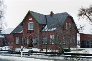 traufständiges Wohnhaus aus Backstein: Straßenfront mit Mittelrisalit, darin unten Eingangsloggia: Giebelseite: links Wirtschaftsgebäude: Vorgarten, Zaun