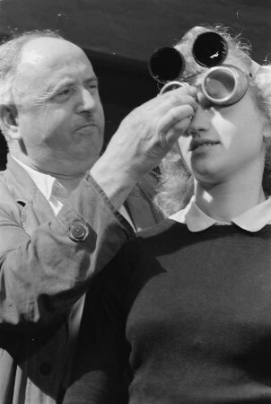 Ein Lehrausbilder paßt einer Schülerin eine Schutzbrille an