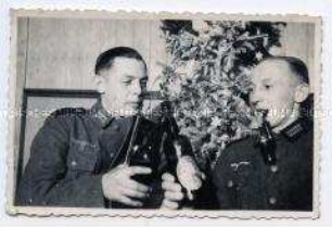 Zwei Heeressoldaten beim Anstoßen mit Flaschen vor einem Weihnachtsbaum