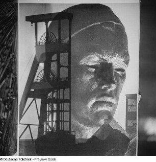 Reproduktion einer Fotografie Wolf Straches, darauf ein Bergwerk mit Förderturm sowie eine Bronzebüste