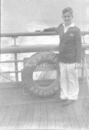 Junge an Deck des Hochseepassagierdampfers "Bremen", neben einem Rettungsring an der Reling stehend