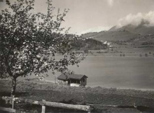 Südtiroler Dolomiten. Bergsee mit Dorf und Wolkentreiben um Gipfel in der Bozener Gegend