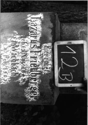 Grabstein 12 (Index: 100090870) Material: Sandstein Zustand: leicht verwittert Maße HxBxT: 157x42x18 cm Beschreibung: Stele, getreppt. Sockel, giebelart. Abschluß mit Verdach. , Schriftfeld m. Rundbogenabs Symbolik: gestelztes giebelartiges Fries: Grabstein 12B