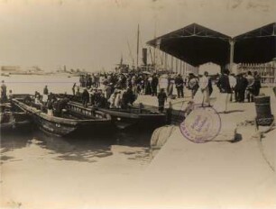 Ägypten. Ankunft der Touristen in Holzruderbooten in einem Hafen (am Nil oder in Alexandria) mit offenen Lagerhallen für Waren, im Hintergrund Schiffe (der Hapag?)