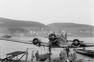 Wasserflugzeug : Männer auf einem Landungssteg, an dem ein Schwimmerflugzeug festgemacht hat.