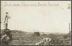 Ein mit Eisenbahnwaggons beladenes Fährschiff auf dem Bosporus beim Verlassen Istanbuls in Richtung des Marmarameeres und des Hafenortes Haidar-Paschar, weitere Boote und Schiffe sowie ein Mann am Ufer im Bildvordergrund links, Blick auf die asiatische Uferseite der Stadt im Hintergrund