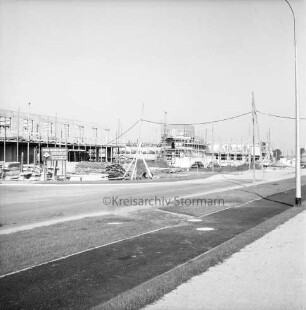 Gewerbegebiet Reinbek/Glinde/Schönningstedt: Bau mehrerer Gewerbebetriebe: vorn Straße mit Gehweg: rechts Straßenlampe: hinten Rohbauten mit Gerüsten: davor Baumaterial: links Bauschild: hinten rechts parkende Pkws