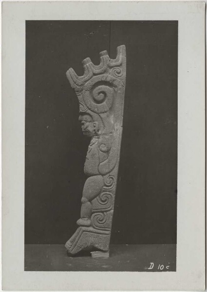 Dancing monkey with the scroll breast ornament of Macuilxochitl, grasping its upwardly curled tail with both hands, crenellated crown. -Palma- Side view.