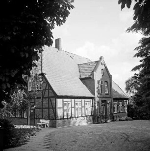 Pastorat: Matthias-Claudius-Straße: Matthias-Claudius-Geburtsstätte [Nachfolgebau von Geburtshaus des Dichters Matthias Claudius]: vor Giebelwand Gartenbank: Plattenweg: Bäume