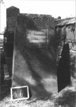 Grabstein 106 (Index: 100114122) Material: Kalkstein Zustand: verwittert Maße HxBxT: 123x85x20 cm Beschreibung: konische Stele, flacher Abschluß, Schriftfeld rechteckig Symbolik: vierzackiges Sternenfries: Grabstein 106