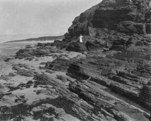 Das Riff : Blick auf die Riffformation am Sandstrand bei Barneville-Carteret. Eine weiß gekleidete Frau an der Küste