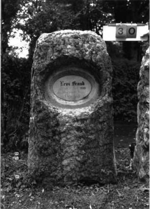 Grabstein 30 (Index: 100101436) Material: Kalkstein, weiße Marmorplatte Zustand: gut Maße HxBxT: 132x64x38 cm Beschreibung: grob stelenhaft behauener Stein, ovale Schriftplatte: Grabstein 30