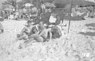 Touristen am Strand unter einem Sonnenschirm sitzend