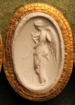 Stehende geflügelte Nemesis mit einer Elle, zu ihren Füßen ein Rad (Daktyliothek, Erstes Mythologisches Tausend)