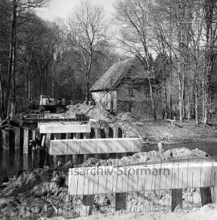 Travebrücke: Landstraße zwischen Nütschau und Schlamersdorf: Nütschauer Weg: Brückenbau: Setzen der Betonpfähle: hinten links Bagger und Erdhaufen, rechts Nütschauer Mühle mit Reetdach: im Hintergrund Bäume
