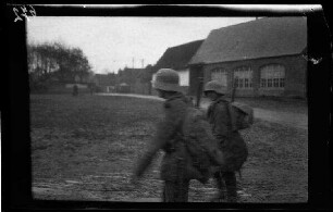 Metz-en-Couture (Dep. Pas-de-Calais, Frankreich): 2 Soldaten mit Sturmhaube und Marschgepäck auf einer morastigen Fläche, im Hintergrund Wohnbebauung und ein landwirtschaftliches Anwesen