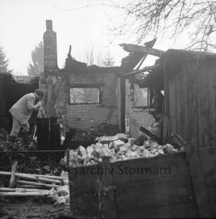 Brand: Sieker Landstraße: Behelfsheim: Brandruine: Innenraum: darin Mauerwerk und verbrannte Gegenstände: hinten rechts im Eingang Polizist: links Brandsachverständiger beim Fotografieren: hinten Bäume