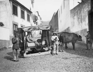 Funchal, Madeira/ Portugal. Tourist in einem von Ochsen gezogenem Schlittentaxi und Einheimische in einer Gasse