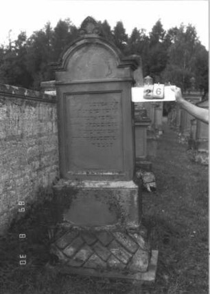 Grabstein 26 (Index: 99609662) Material: Sandstein Zustand: stark verwittert, teilweise Textverlust Maße HxBxT: 209x72x34 cm Beschreibung: Stele, eingezogener Rundbogenabschluß mit Verdachung, Mittelpalmette, Schriftfeld rechteckig eingetieft, getreppter Sockel, unten Rusticaimitat: Grabstein 26