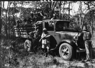 Lastkraftwagen : Ein Lastkraftwagen im Wald. Darauf Gepäck und eine Gruppe Menschen.