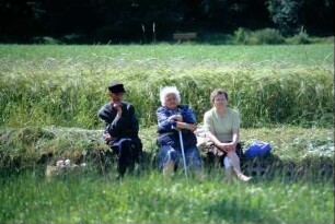 zwei Frauen und ein Mann sitzen an einem Wiesenrand