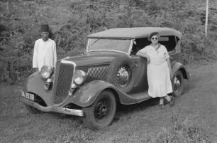 Doppelportrait : Eine Frau und ein Mann stehen neben einem Automobil.
