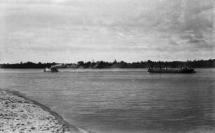 Schiffe auf dem Mbini : Den Mbini stromabwärts: Ein Schiff, das mit schweren Edelholzblöcken beladen ist, wird zum Ladeplatz eines Holzdampfers gezogen.