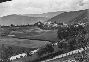 Dorf : Ein Dorf mit Kirche umgeben von Ackerland in einem Hochtal. Im Hintergrund Hügelketten mit Bergwald, im Vordergrund ein Bach