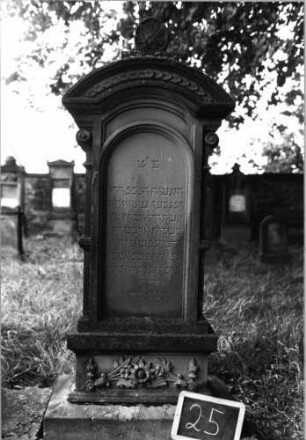 Grabstein 25 (Index: 100080686) Material: Sandstein Zustand: gut Maße HxBxT: 166x47x24 cm Beschreibung: ausgezog. Rundbogenabschl. m. Verdach. u. Mittelakroter, Schriftfeld eingetieft Symbolik: Blumen/Blätter auf Sockel; Voluten unter Abschl. ansatz; Fries: Grabstein 25