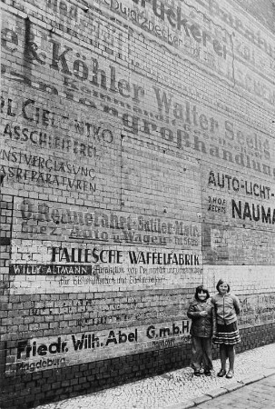 Zwei Mädchen vor einer Hauswand mit Reklameaufschriften