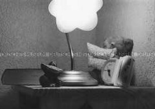 Nachttisch mit Lampe, Wecker, Buch und Kuscheltier (Altersgruppe bis 14)