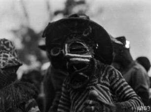 Tänzer : Ein Tänzer mit Maske und gestrickter Kleidung. Links ein weiterer.