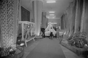 Besucher der Leipziger Herbstmesse 1955 betrachten drapierte Stoffbahnen
