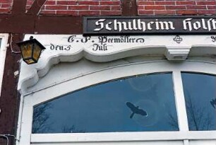 Dorfstraße 10: Schullandheim: traufständiges Fachwerkhaus mit Reetdach: Giebelseite Wirtschaftstrakt: ehemaliges Scheunentor: Detailaufnahme: Oberlicht, darüber Schriftzüge "Schulheim im Hol[stentor]", G.F. Peemöller den 5. Juli [Anno 1856]