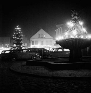 Marktplatz: Adventsbeleuchtung: vorn rechts Gänseliesel-Brunnen, links Tannenbaum: dazwischen parkende Pkws: hinten Wohn- und Geschäftshäuser an Hindenburgstraße: Abend