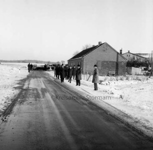 Straßenbau: Kreisstraße Richtung Wakendorf (Kreis Segeberg): Einweihung und Freigabe: Begehung der Straße durch Landrat Wennemar Haarmann, Bürgermeister Adolf Grimm, Kreisausschussmitglieder, Gemeindevertreter sowie Vertreter des Kreises Segeberg und der Gemeinde Wakendorf: hinten links mehrere Pkws: hinten rechts Bauerngehöft: hinten Wald: Winter