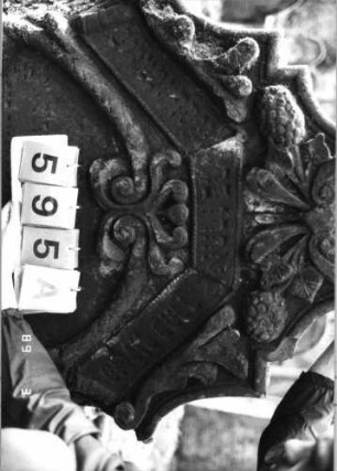 Grabstein 595 (Index: 99753098) Material: Sandstein Zustand: verwittert mit Textverlust Maße HxBxT: 126x97x18 cm Beschreibung: in geschwung. Treppen eingezog. Rundbogenabschl. , ovales Schriftfeld eingetieft Symbolik: Muschel, Pinienzapfen, Blätter, Ranken, Schriftband, Voluten: Grabstein 595A