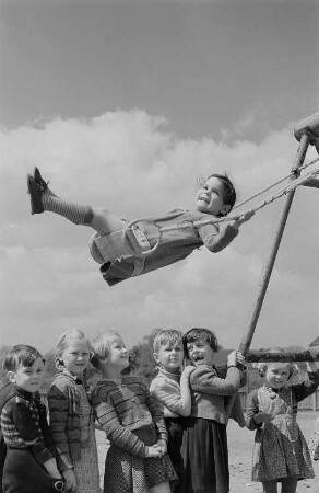 Ein schaukelndes Mädchen und wartende Kinder
