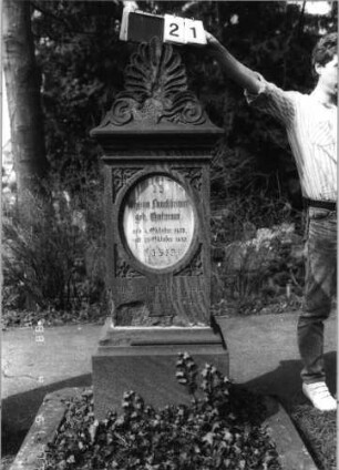 Grabstein 21 (Index: 99792914) Material: Sandstein und Marmor Zustand: beschädigt Maße HxBxT: 162x52x34 cm Beschreibung: Stele, Sockel profiliert, Giebel mit Akroter, Schriftfeld eingetieft, stehendes Oval, eingesetzte Textplatte Symbolik: Efeublätter Besonderheit: Schrift vergoldet: Grabstein 21